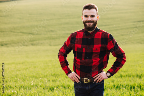 Young bearded agronomist standing in cultivated wheat crops field