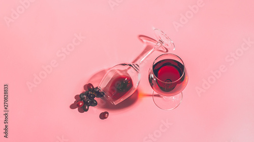 A glass of red wine on the table is turned upside down and a bunch of grapes on gentle pink background. Selective focus.