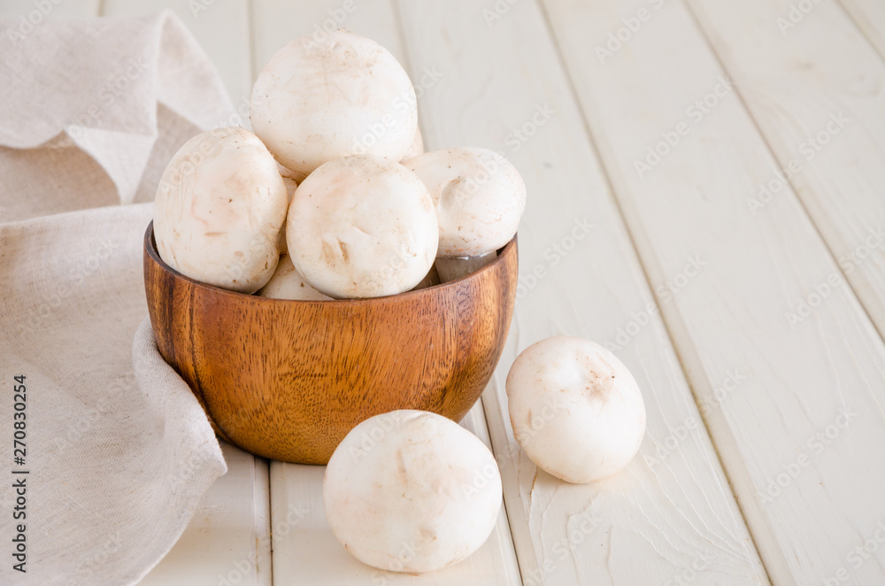 Fresh raw champignons in a wooden bowl on a white background with space for text.