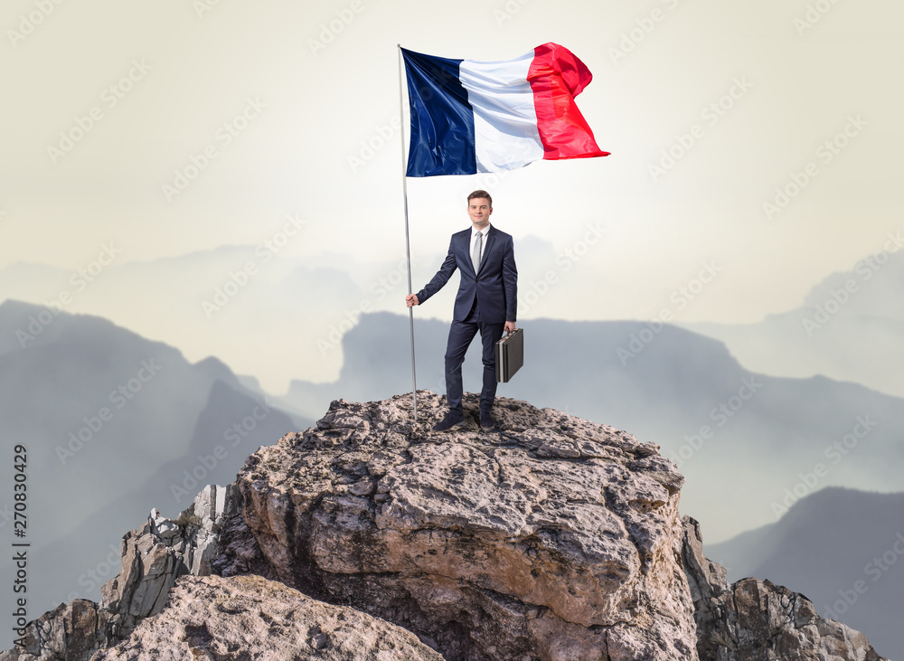 Obraz premium Successful businessman on the top of a mountain holding France victory flag 