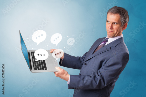 Man holding laptop with a few speech bubble symbols  