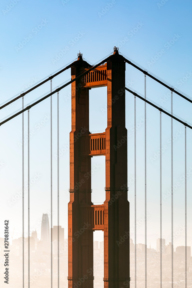 Fototapeta premium Rise Above - The iconic north tower of the Golden Gate Bridge is backed by a the city of San Francisco as the morning hazes clears.