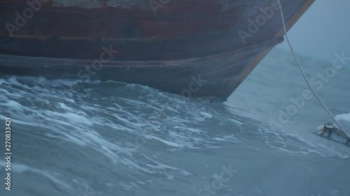 Closeup boat bow drifting in the wavy sea over cloudy dark sky background. Cinematic dramatic footage of boat in restless sea water and sky before the storm in early morning
