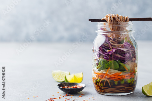 Healthy asian salad with noodles, vegetables, chicken and tofu in glass jars. Grey background. Copy space.