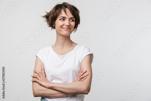 Image of optimistic woman in basic t-shirt smiling and looking aside while standing with arms crossed
