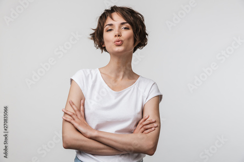 Image of happy woman in basic t-shirt looking at camera while standing with arms crossed