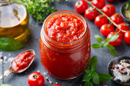 Traditional tomato sauce in a glass jar with fresh herbs, tomatoes and olive oil. Copy space. Slate background. photo