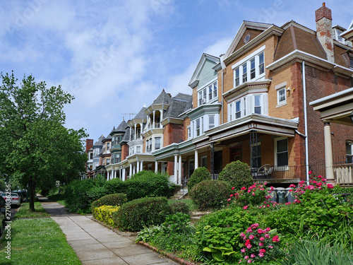 Row of large old brick houses with front porches and gardens