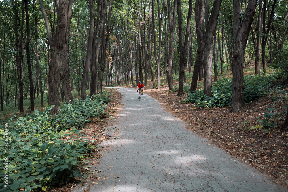 A cyclist rides on a road bicycle on road in woods. A cyclist rides on a road bicycle on road in woods.