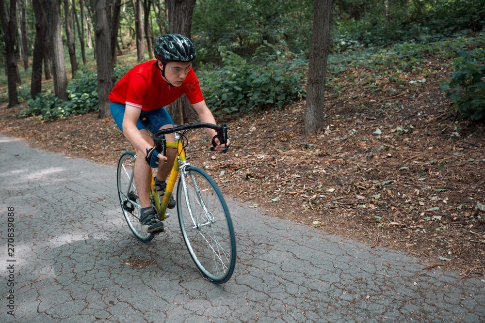 Fototapeta premium A cyclist rides on a road bicycle on road in woods.