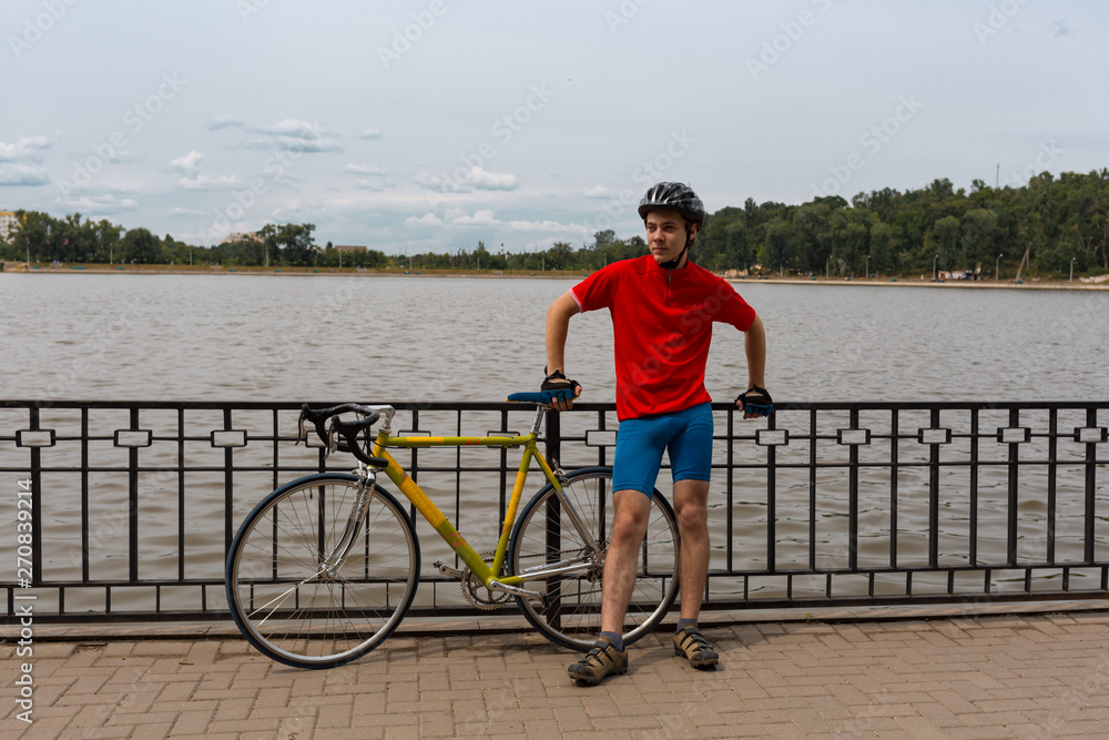 Athlete stands next to his road bike on waterfront of lake. Natural background.