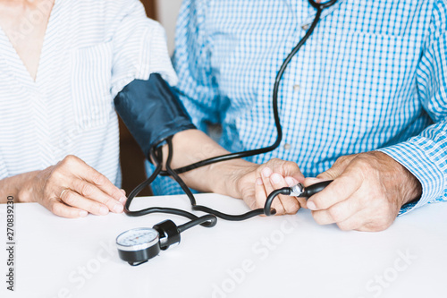The therapist male hands in blue shirt with a classic tonometer measuring blood pressure of an woman in home room on white table.