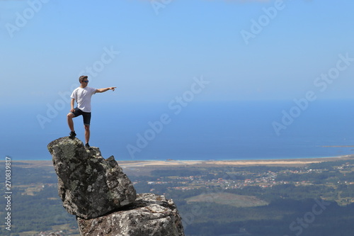 ISOLATED BOY POINTING FROM THE TOP OF A ROCK NEAR THE OCEAN ON SUMMER HOLIDAY