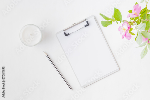Flat lay blogger or freelancer workspace with a clipboard, pink flowers on a white background