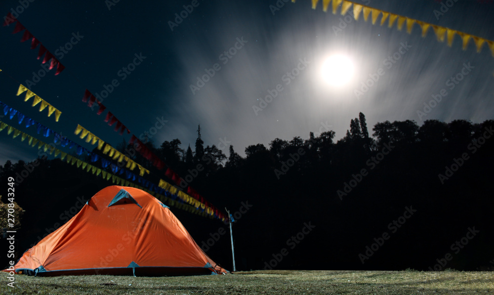 A tent set up under the night sky with moon rise.