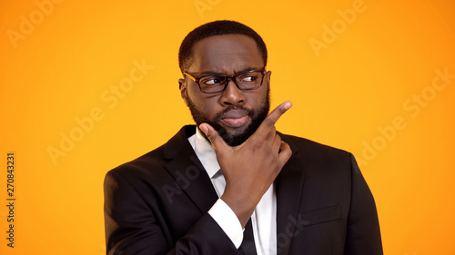 Suspicious african-american businessman in glasses considering options, dilemma photo