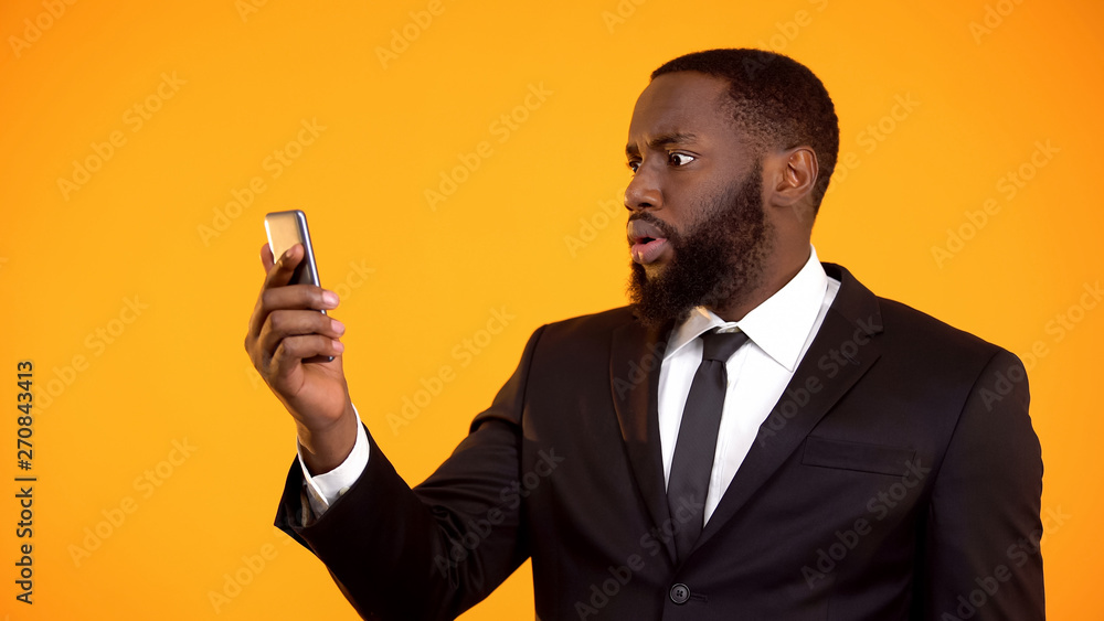 Shocked african-american male reading email on phone, mobile app, astonishment Shocked african-american male reading email on phone, mobile app, astonishment