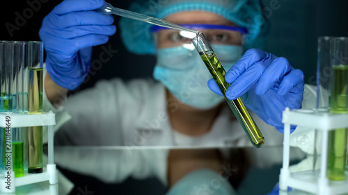 Tableau sur toile Biologist adding oily substance in tube with green plant, biofuel extraction