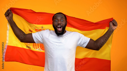 Cheerful black sport fan holding Spanish flag cheering for national team victory
