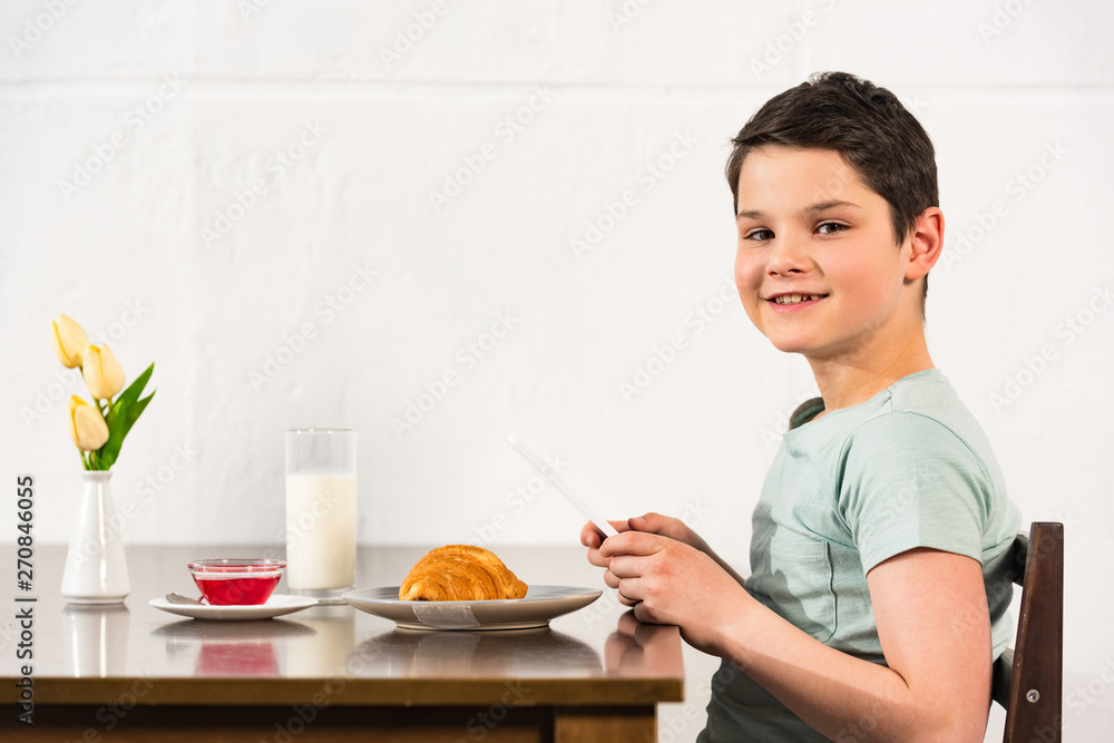 smiling boy using digital tablet during breakfast in kitchen smiling boy using digital tablet during breakfast in kitchen