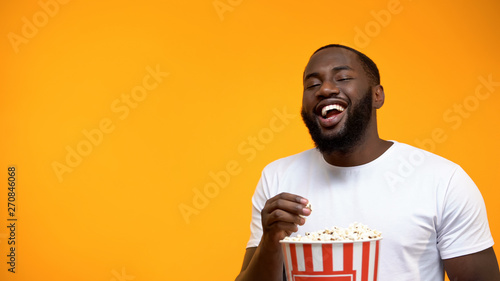 Cheerful Afro-American man eating popcorn and laughing out loud, comedy show