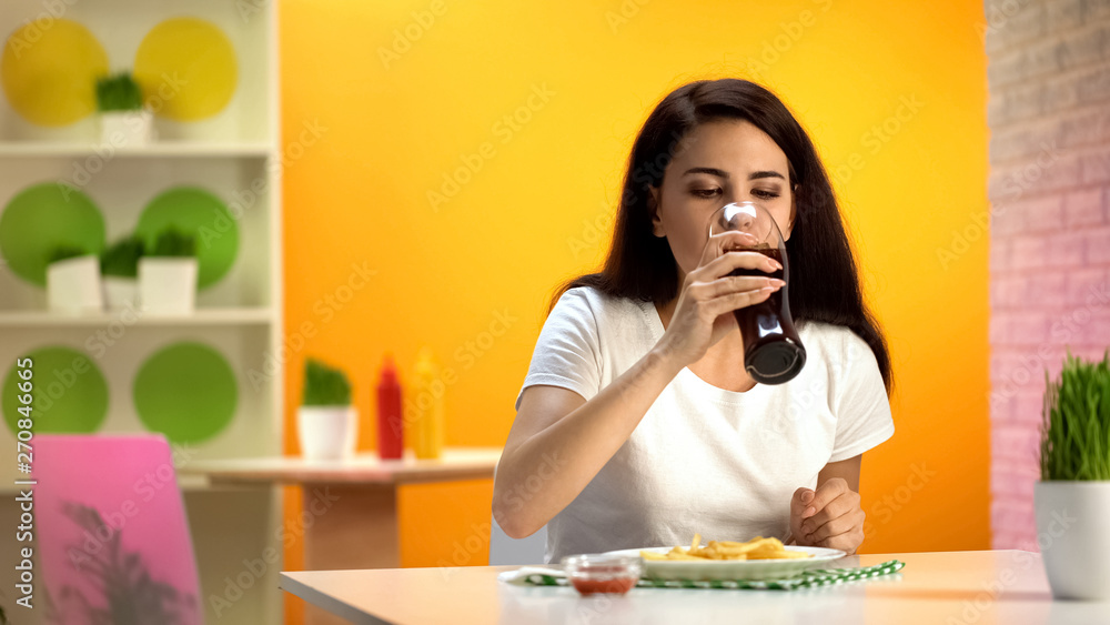 Beautiful lady drinking soda water, french fries on plate, fast food cafeteria