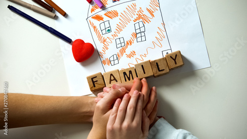 Kid holding hand of adult person  family word made from cubes on house picture