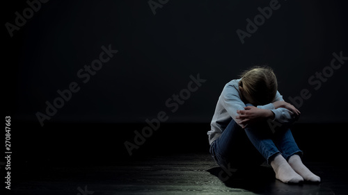 Obraz na płótnie Depressed little girl sitting alone in dark room loneliness and bullying concept