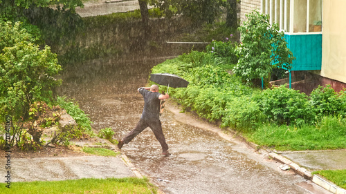 A man with an umbrella jumps over a puddle during heavy rain in summer