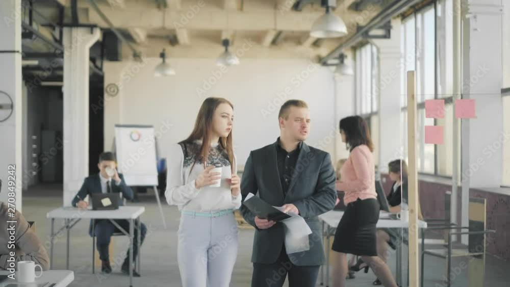 Two employees a man and a woman walk around the office, communicate and discuss business processes. Office life. Coworking Two employees a man and a woman walk around the office, communicate and discuss business processes. Office life. Coworking
