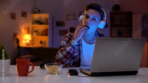 Canvas-taulu Excited teenage boy playing computer game and eating snack, leisure activity