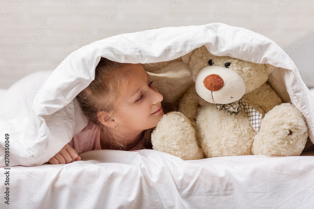 adorable little child girl playing with teddy bear in bed in morning. baby with a teddy bear under the covers adorable little child girl playing with teddy bear in bed in morning. baby with a teddy bear under the covers