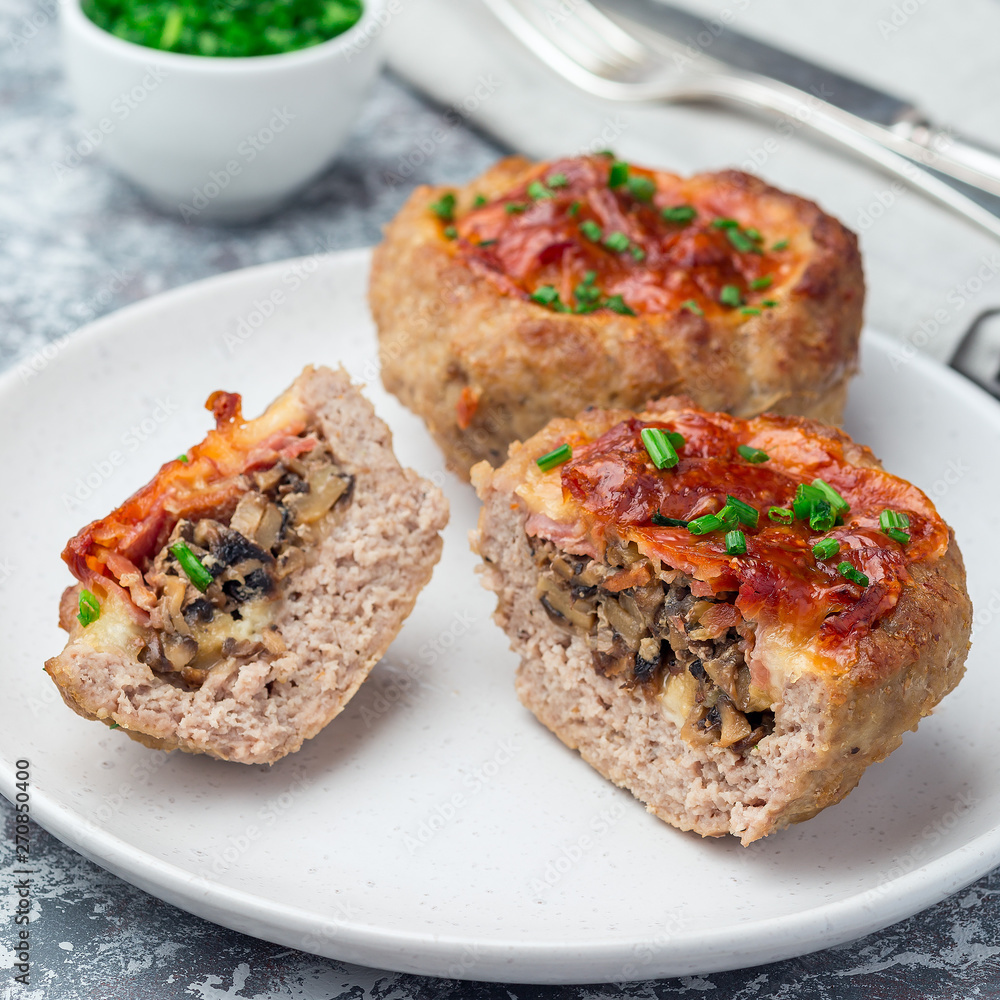 Low carb paleo meat cups, stuffed with champignons, bacon and cheese, garnished with green onion, on plate, square format Low carb paleo meat cups, stuffed with champignons, bacon and cheese, garnished with green onion, on plate, square format