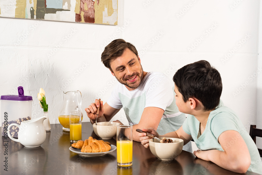 smiling father and son having breakfast and looking at each other in kitchen