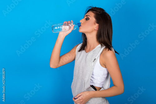 Beautiful teen girl holding bottle of water, smiling and drinking fresh water