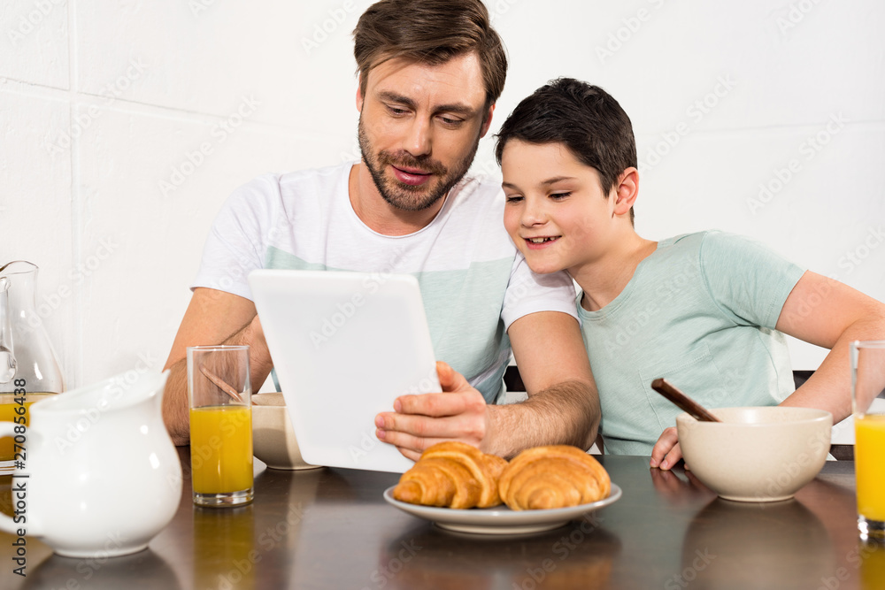 smiling dad and son using digital tablet during breakfast