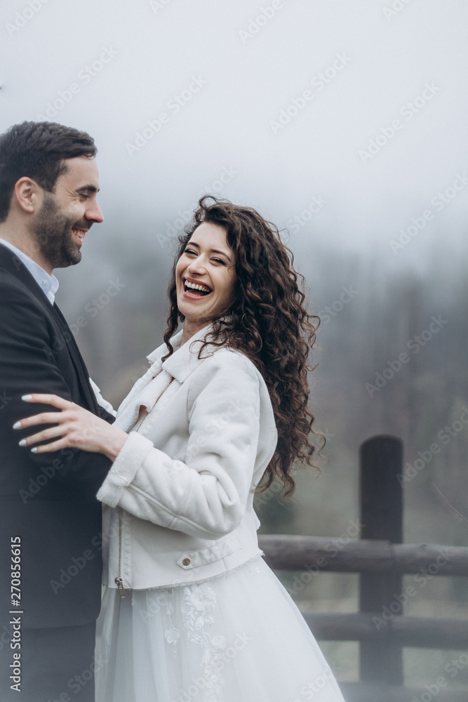 Stylish cute couple of attractive men and women hugging and kissing while walking in misty weather in the mountains Stylish cute couple of attractive men and women hugging and kissing while walking in misty weather in the mountains