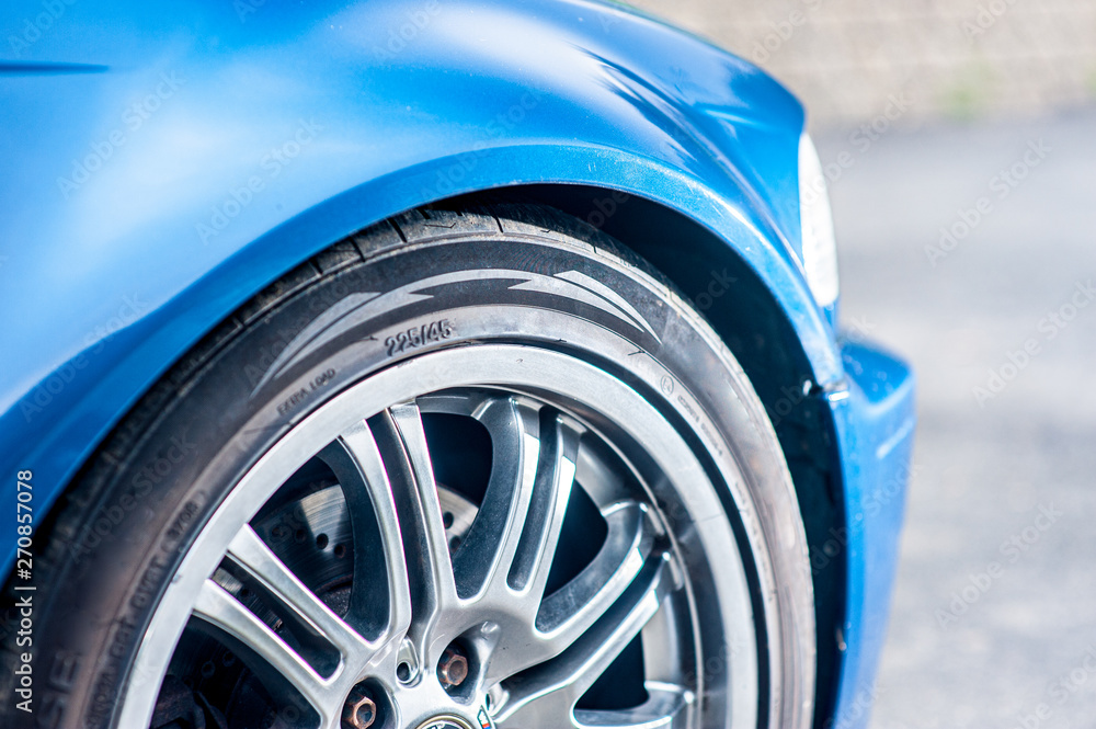 Details of the front right wheel of a fast, blue car.