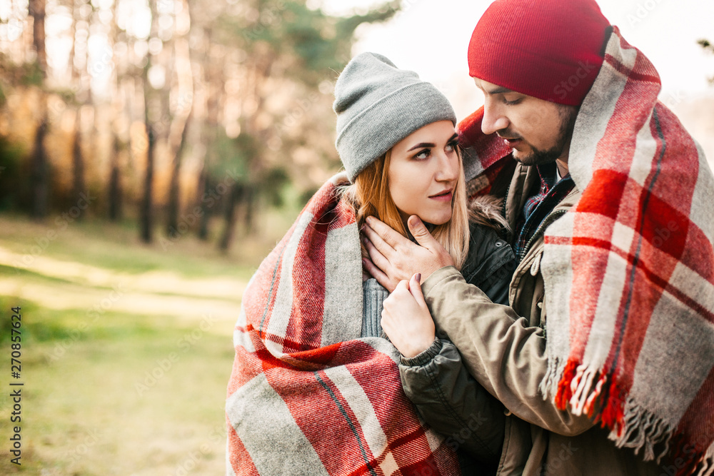 Couple huggings travelers covered with plaid in the forest. Concept of trekking, adventure and seasonal vacation. Couple huggings travelers covered with plaid in the forest. Concept of trekking, adventure and seasonal vacation.