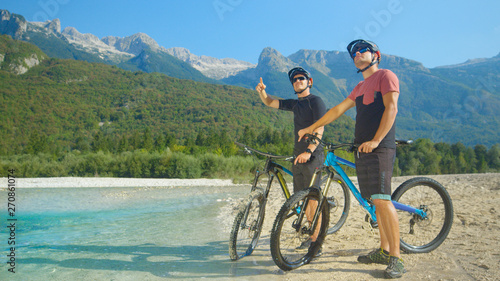 Young guys on ebikes stand by the river and look at the beautiful landscape.