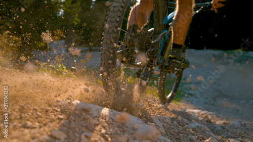 CLOSE UP, DOF: Mountain biker kicking up dust and rocks while braking hard photo