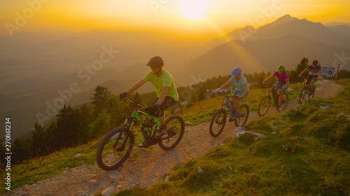 AERIAL: Golden evening sunbeams shine on the mountain bikers riding up a trail.