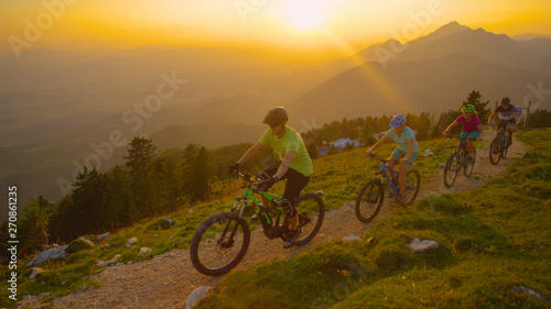 DRONE: Cheerful tourists riding mountain bicycles up a scenic trail at sunset.