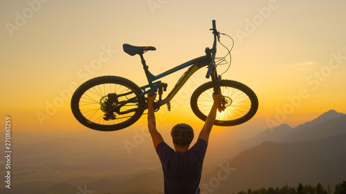 CLOSE UP: Unrecognizable man lifts his bicycle in the air at golden sunset.
