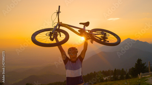LENS FLARE Morning sun rays shine on the excited man lifting his bike above head