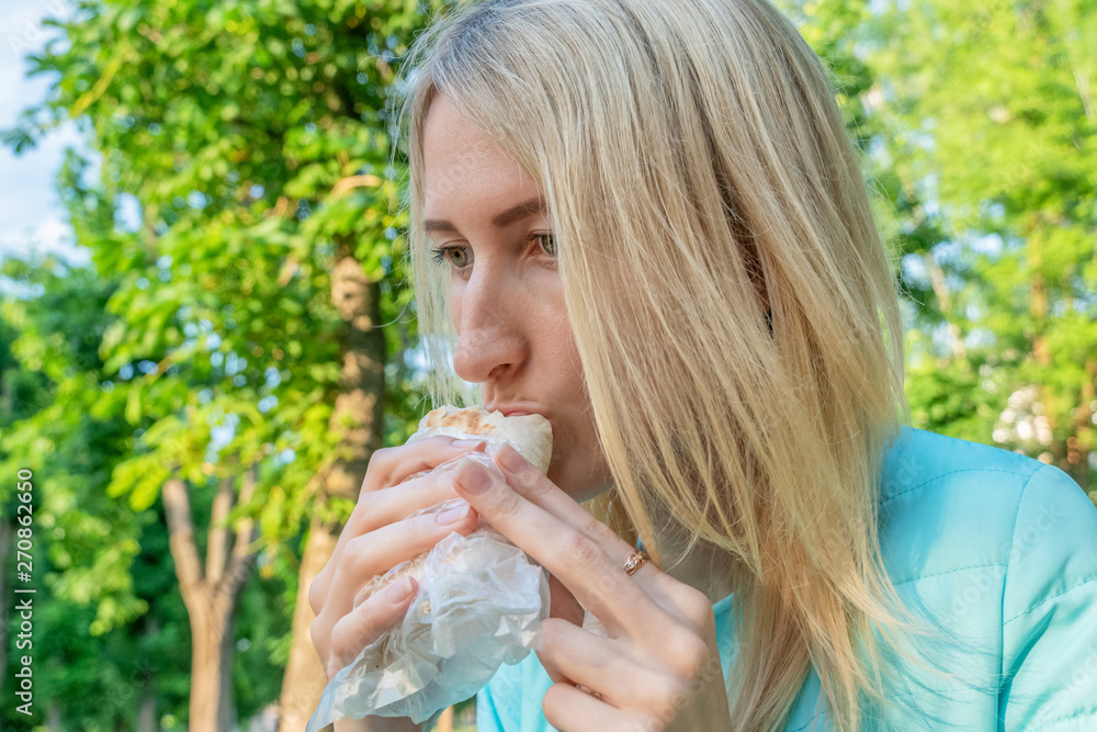 Blonde girl eating shawarma outside on a sunny spring day. Fast food Blonde girl eating shawarma outside on a sunny spring day. Fast food