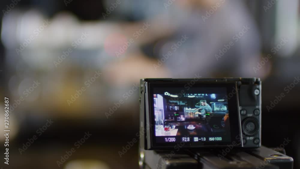 Panning close-up shot of camera set on counter and filming male barista, who is demonstrating different features of professional coffee machine for video tutorial, looking towards camera and gesturing Panning close-up shot of camera set on counter and filming male barista, who is demonstrating different features of professional coffee machine for video tutorial, looking towards camera and gesturing