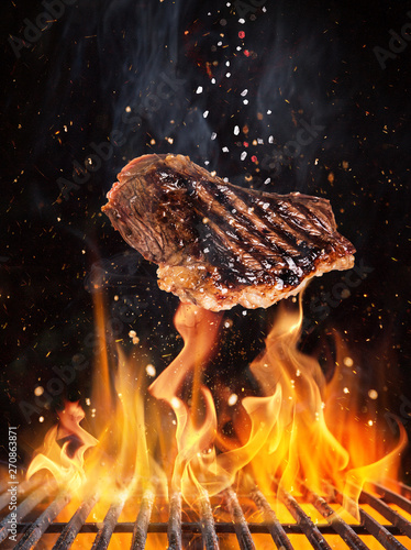 Tasty beef steaks flying above cast iron grate with fire flames. Freeze motion barbecue concept. © Lukas Gojda