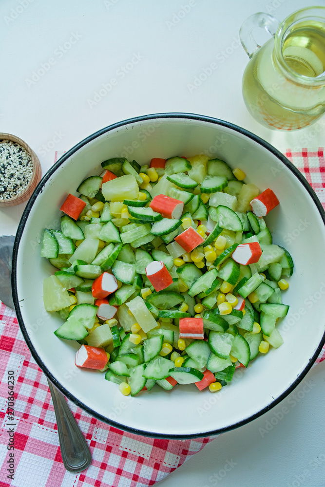 Salad with corn, crab sticks, cucumbers in a white bowl on a white background. Vegetarian salad. Cooking process. Salad with corn, crab sticks, cucumbers in a white bowl on a white background. Vegetarian salad. Cooking process.