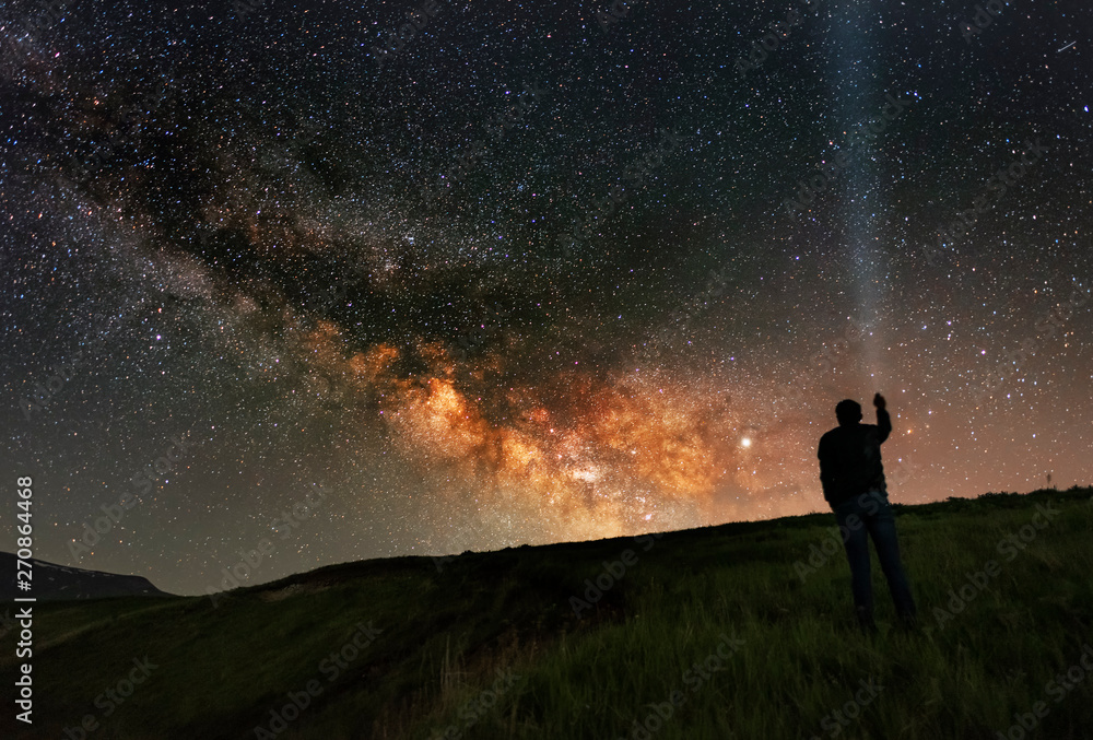 Fototapeta premium Beautiful starry night, man silhouette stands on in the hill and looks at the Milky Way galaxy.